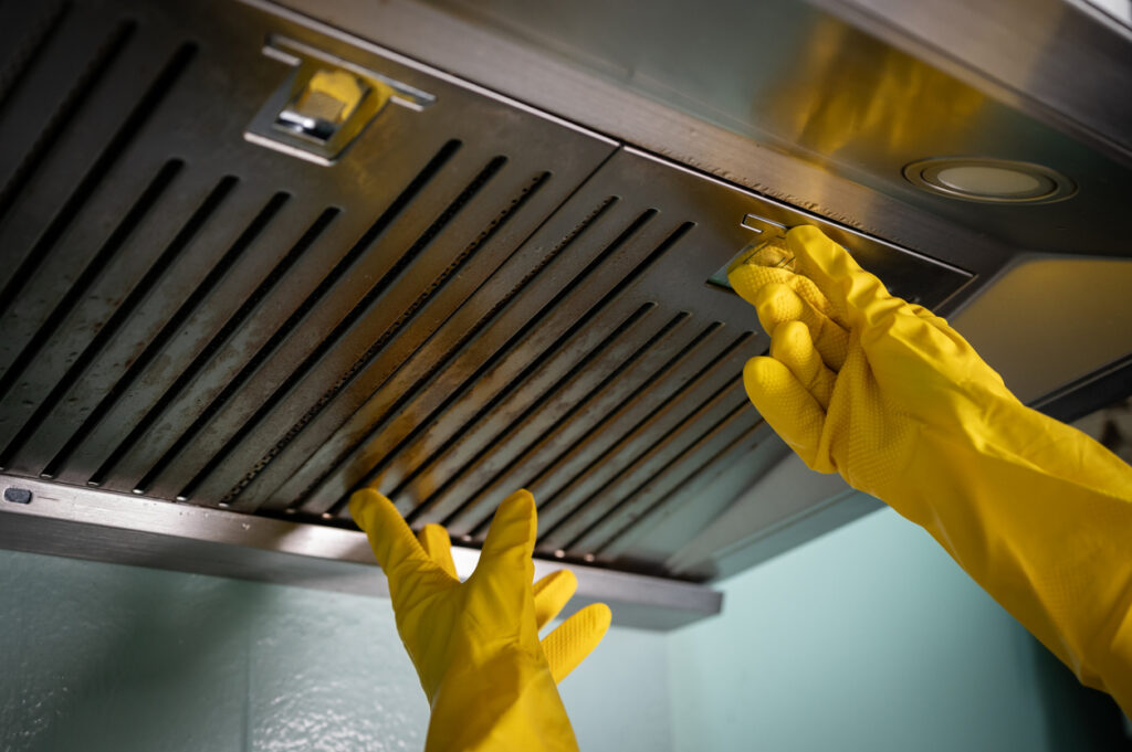 Two gloved hands unlatching a hood vent filter above a stove
