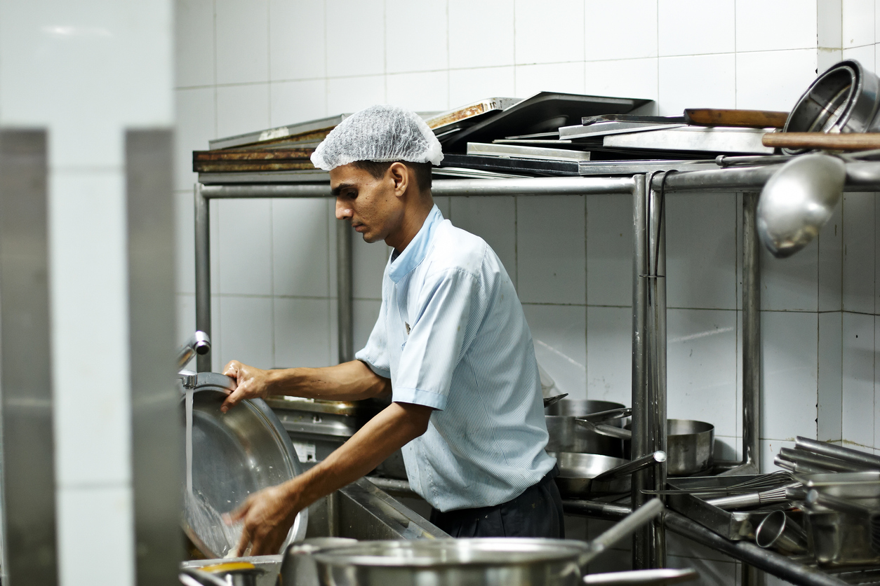 Hotel worker washing dirty dishes in commercial kitchen