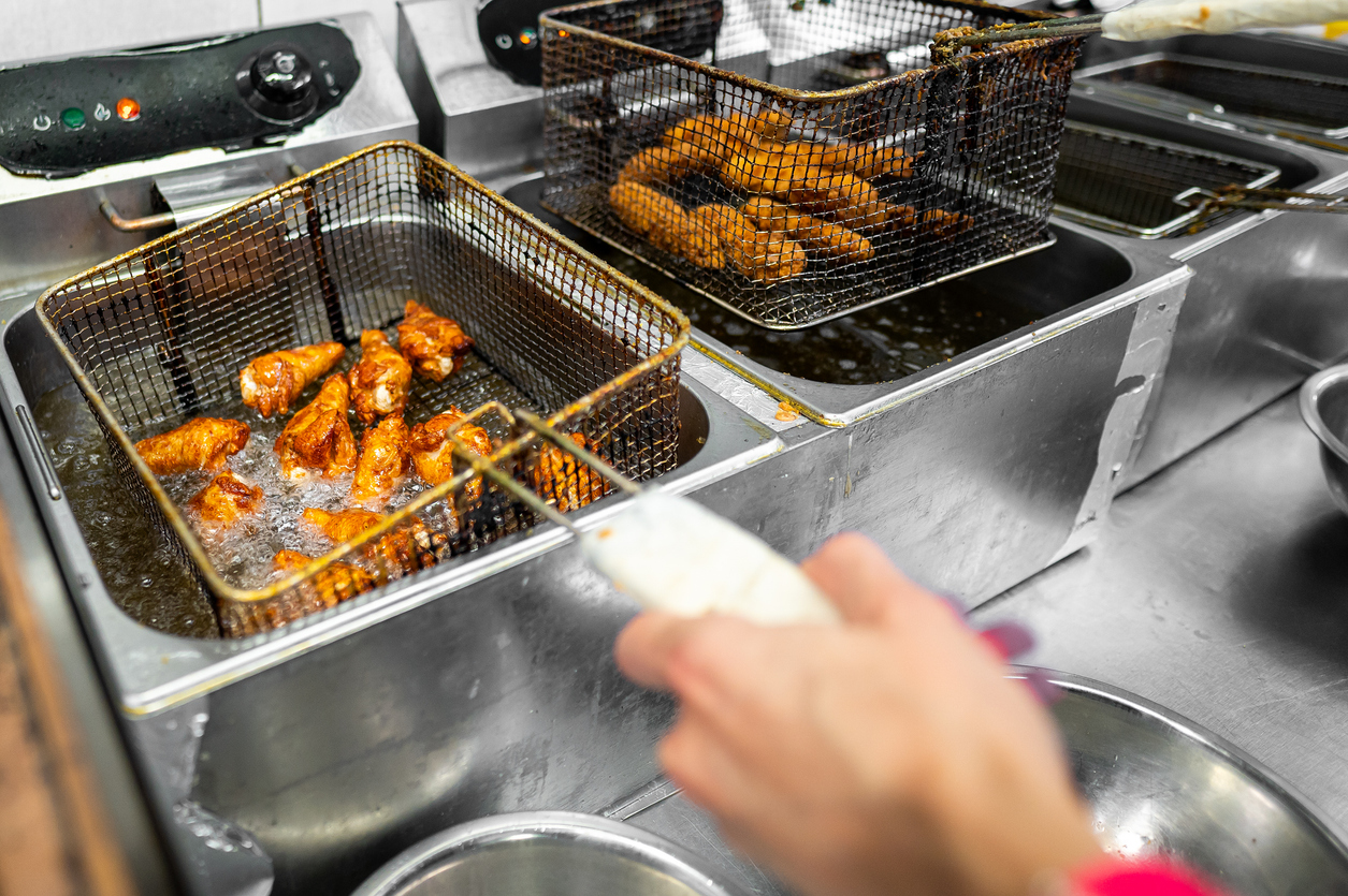 Close-up of crispy fried chicken wings being taken out of a deep fryer by a person in a commercial kitchen