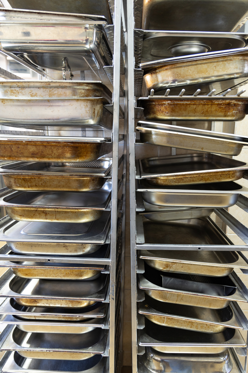 Empty metal kitchen trays arranged on shelves in a professional kitchen