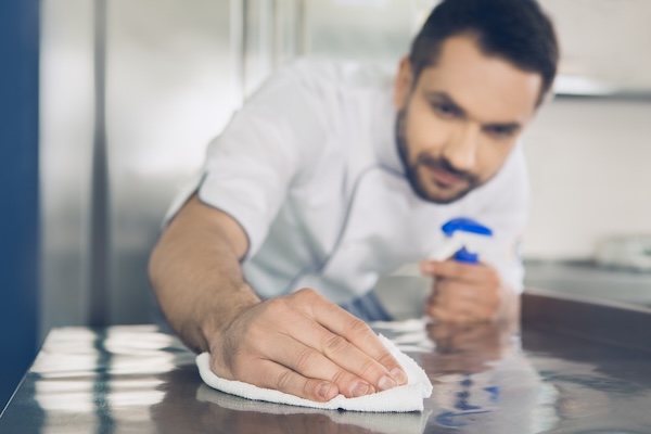 A chef working in a restaurant shows how to remove built-up grime during deep cleaning by drying kitchen surfaces with a cloth after they're cleaned and rinsed