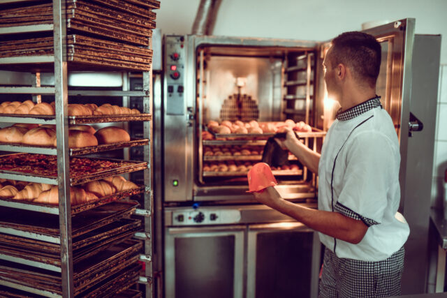 Careful Baker Operating Trays With Pastries And Oven