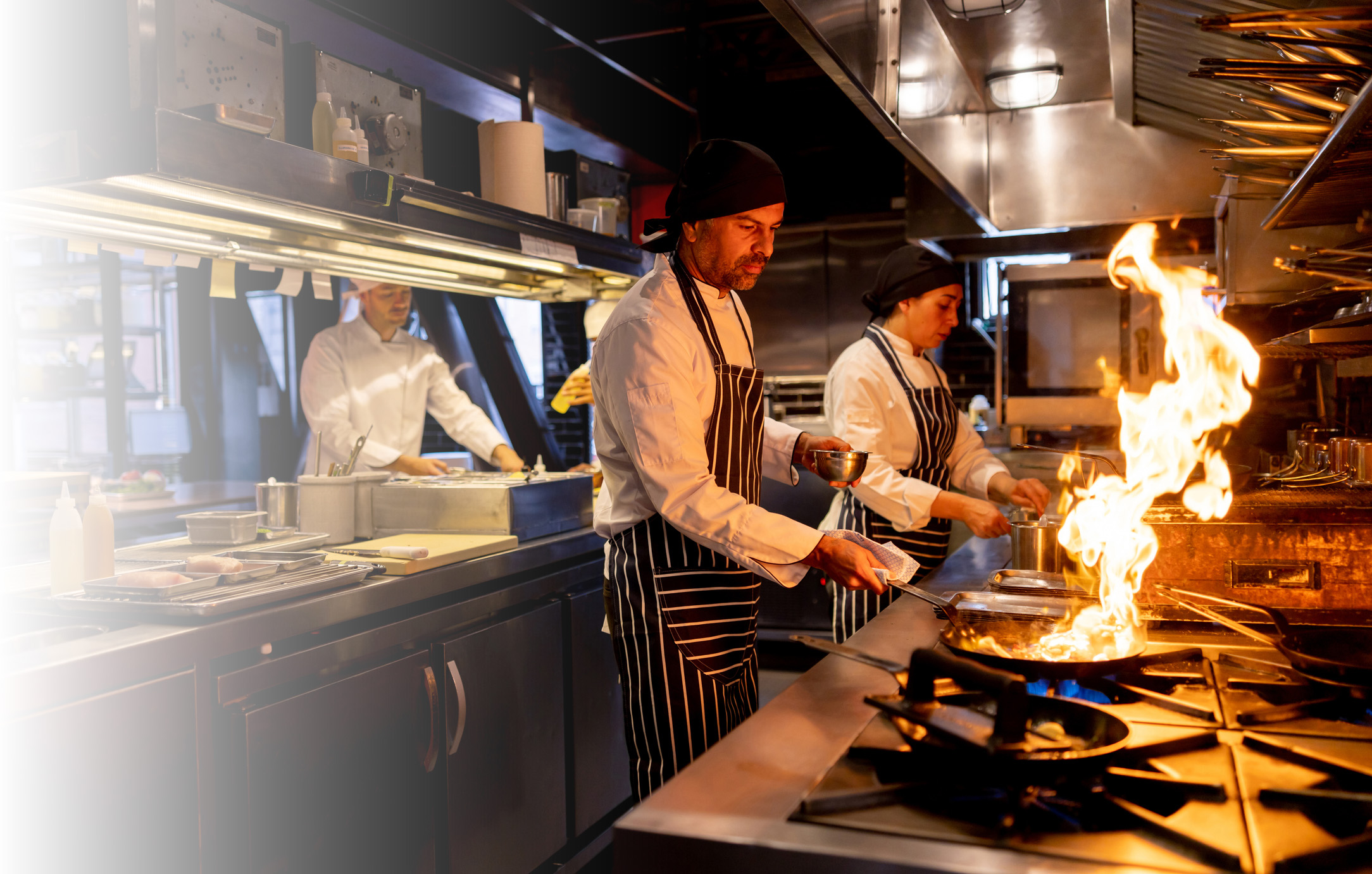 Chef cooking at a restaurant and flaming the food on a pan - food and drink concepts