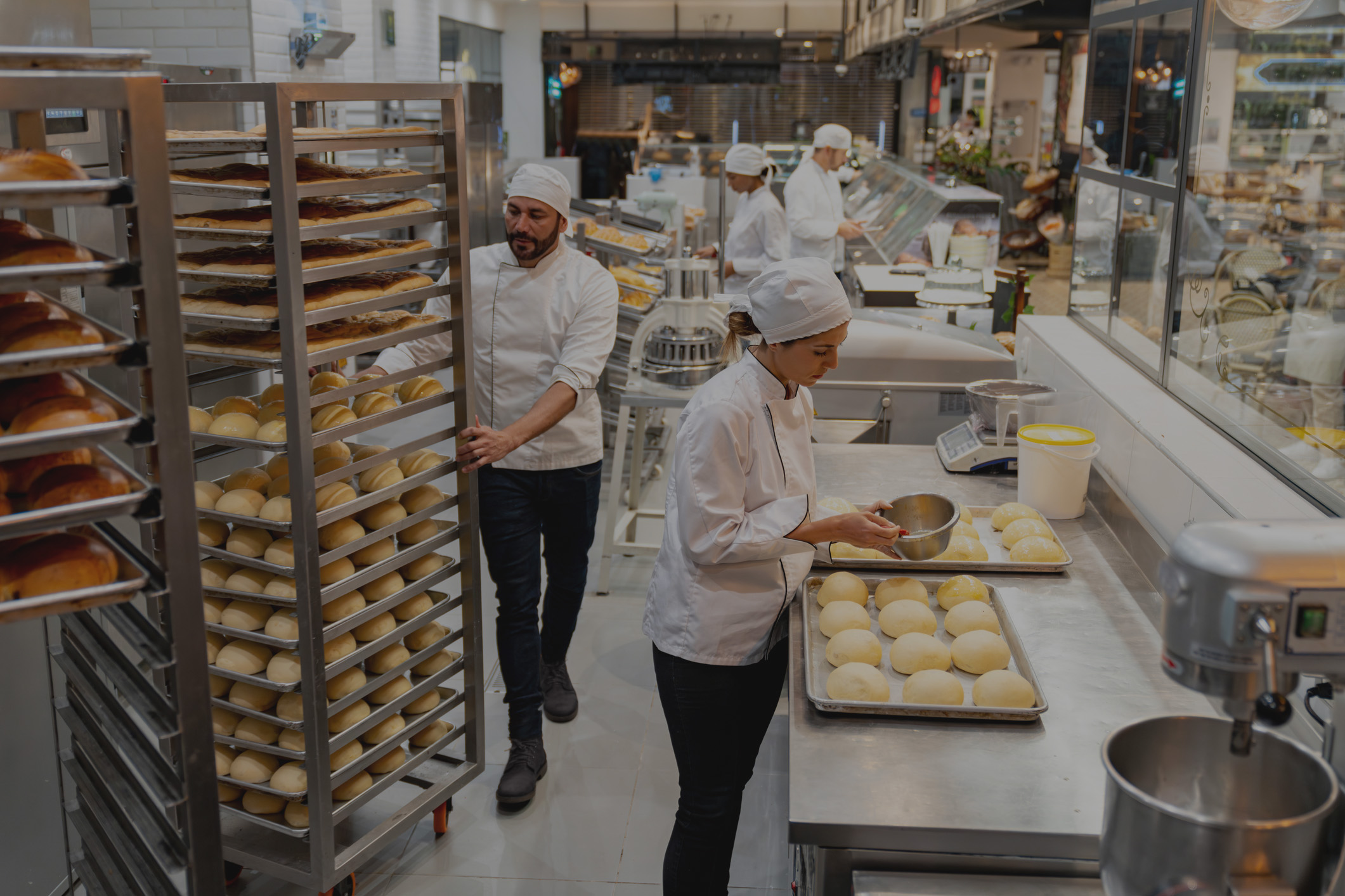 Group of employees working at a bakery baking fresh bread, wheeling a tray of baked goods