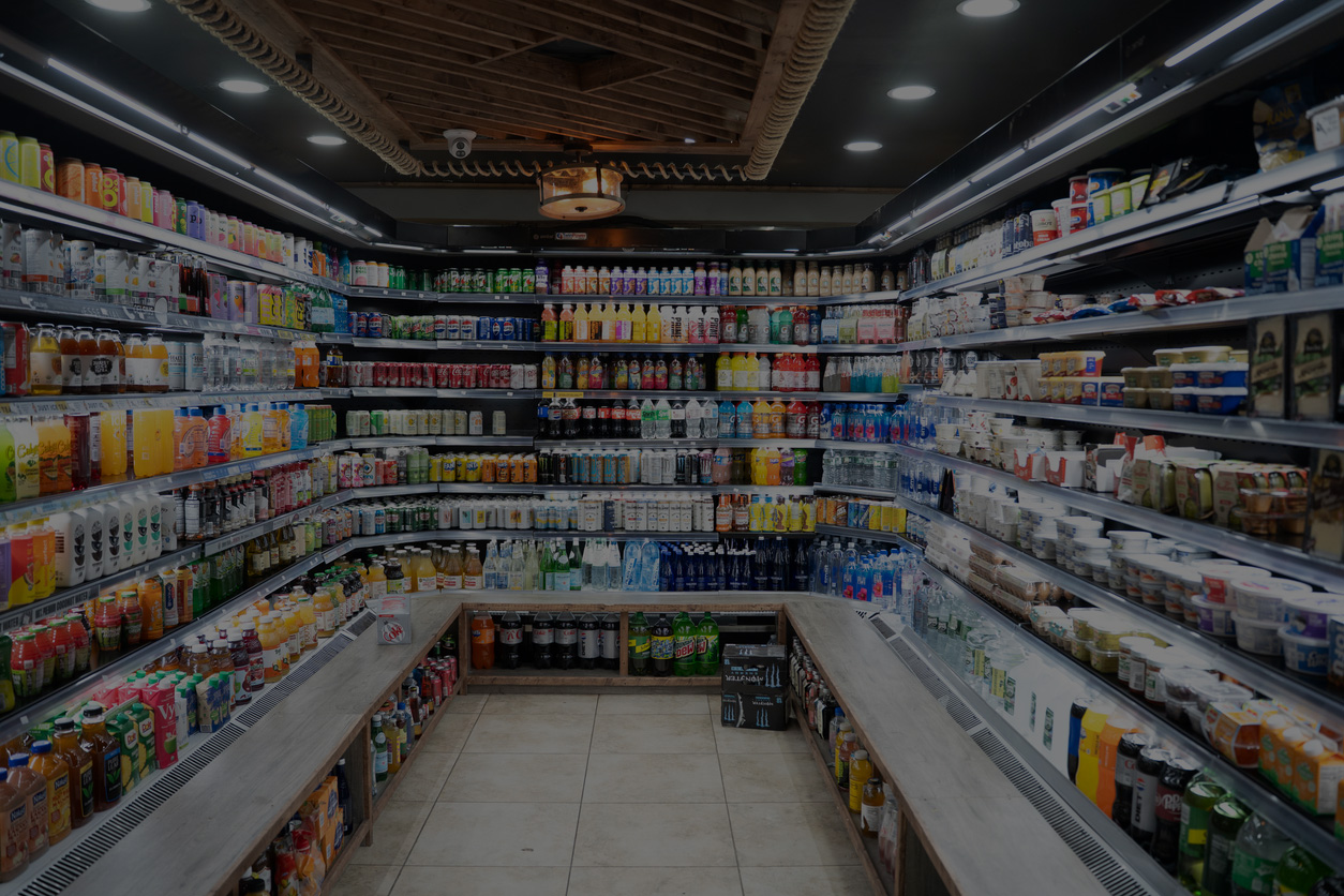 A wide-angle view of a well-lit urban market featuring long aisles of glass-door refrigerators stocked with a variety of cold beverages and drinks